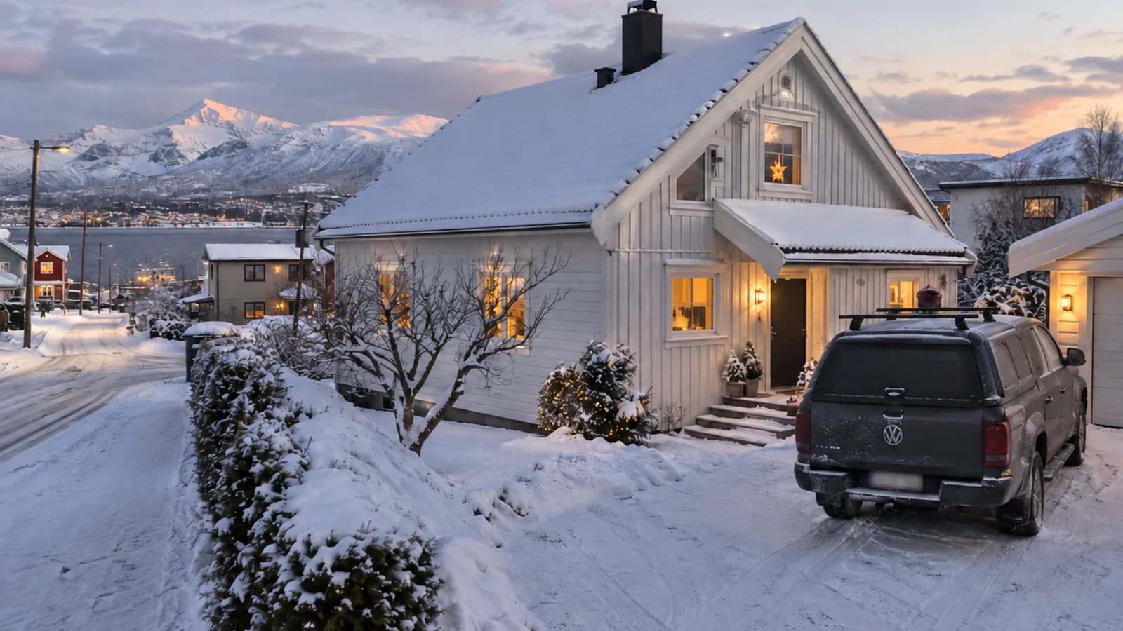 White detached house in snow with a pickup truck in the driveway and snow-covered mountains behind